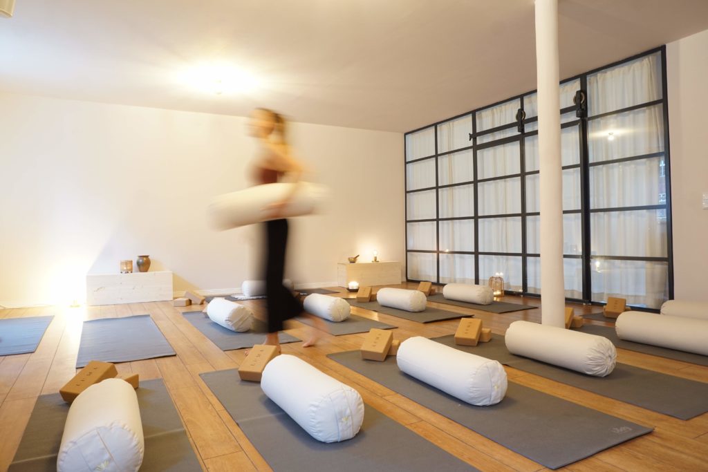 Ein minimalistischer, stilvoller, stimmungsvoller Yogaraum wird von einer Person für den nächsten Yogakurs vorbereitet.